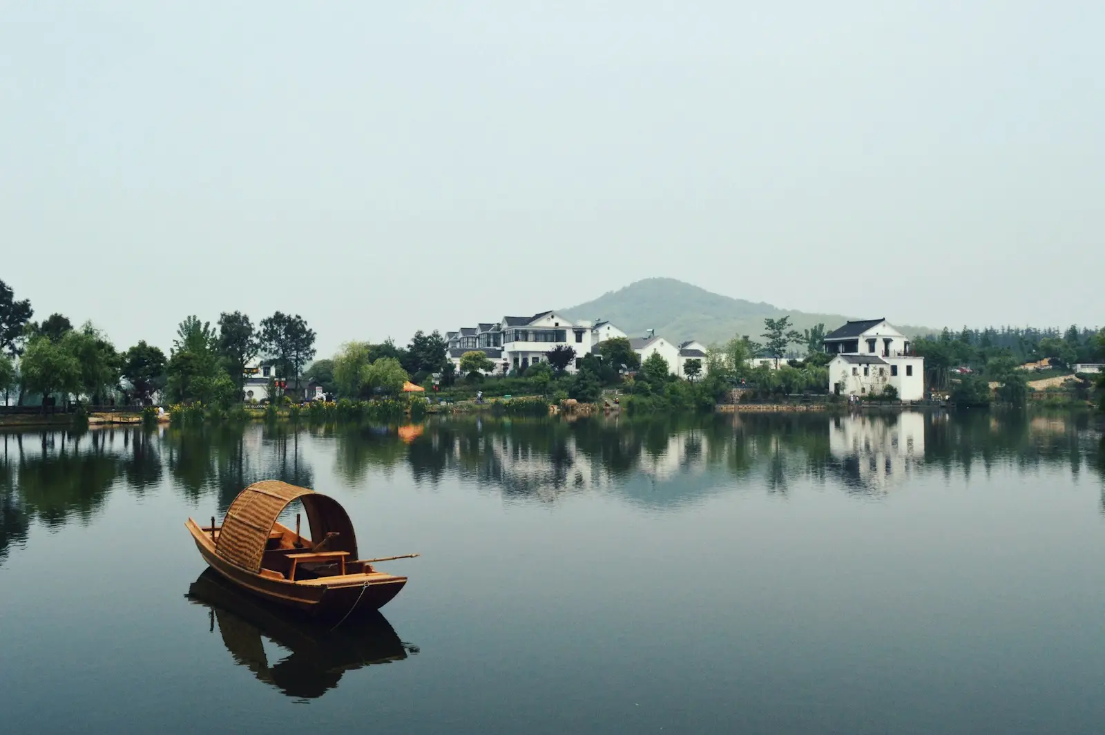 brown wooden boat on body of water overlooking houses by the shore at daytime