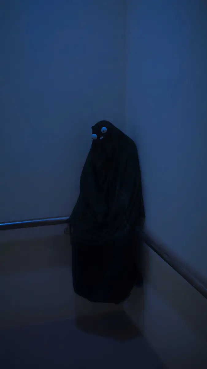 person in black robe standing beside white wall